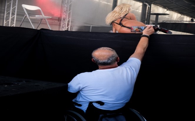 A man user of wheelchair at a show, capturing a lady dancing.