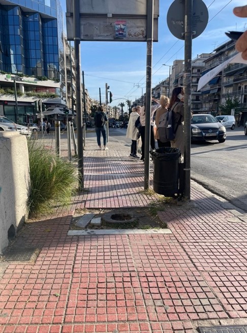 A destroyed sidewalk in the centre of Athens, a trash bin and a road sign.