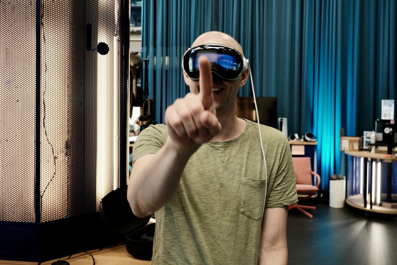 A person wearing an XR headset stands indoors and reaches one hand toward the camera.