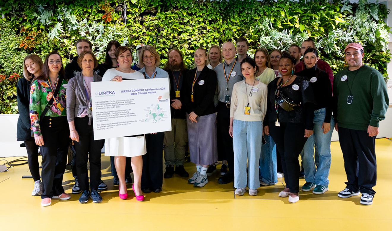 Ryhmäkuva U!REKA CONNECT Conference 2025 -tilaisuudesta: joukko osallistujia seisoo vihreän kasviseinän edessä, ja etualalla pidetään konferenssin “Made Climate Neutral” -julistetta.